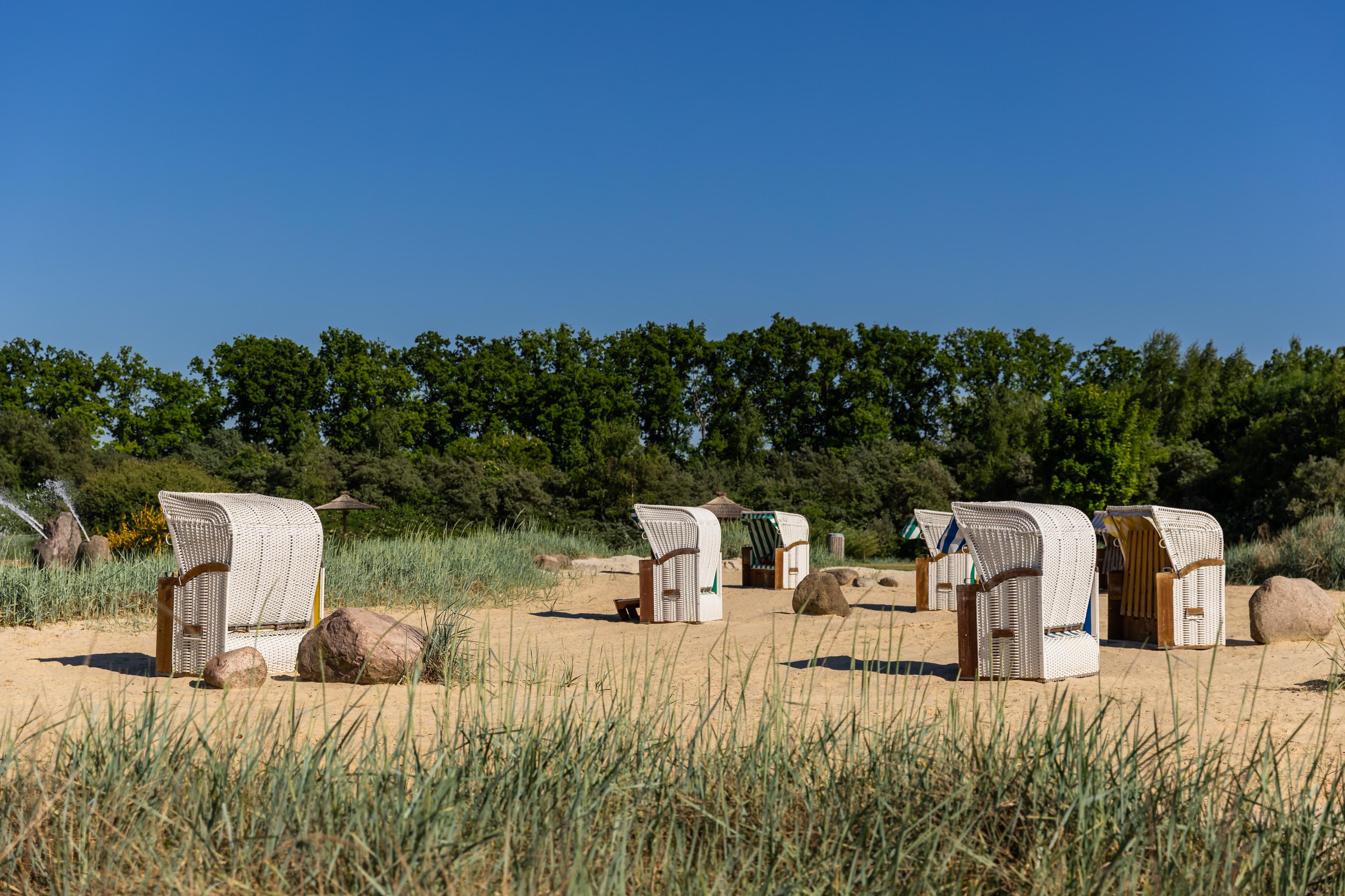 Zu sehen ist der Strandbereich des Naturbades in Olfen mit vielen Strandkörben, Schilf und viel Natur.