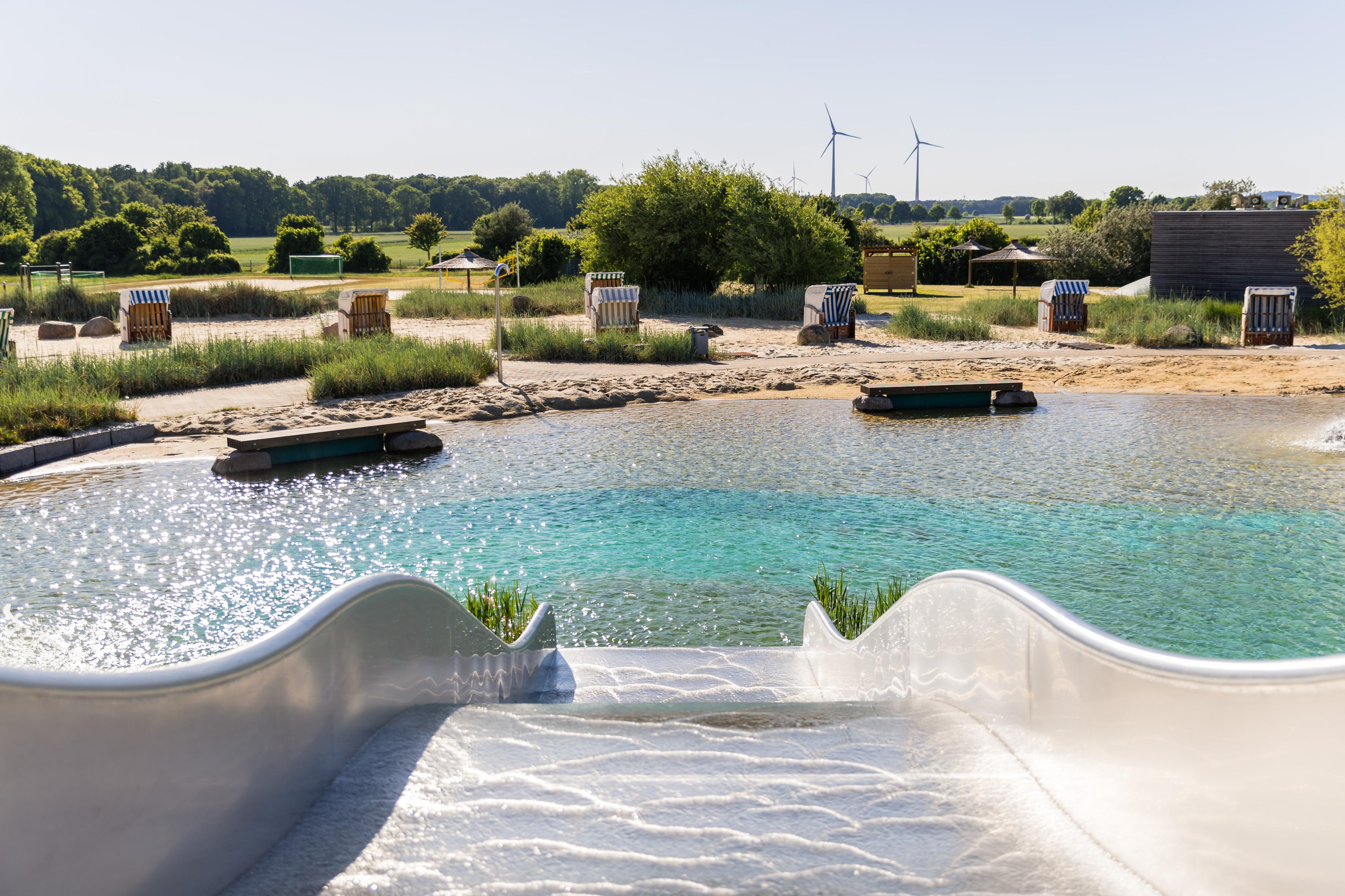 Im Vordergrund ist die Rutsche des Naturbades zu sehen, welche direkt ins Nicht-Schwimmer-Becken führt.