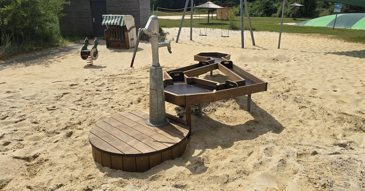 Ein Matschtisch aus Holz mit einer Pumpe mitten im Spielbereich des Naturbades.