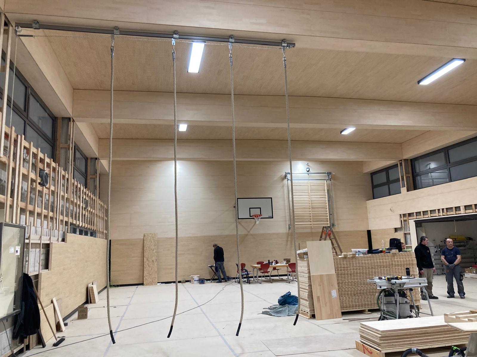 Die Geestturnhalle hat neue Holzwände und eine neue Holzdecke. Auf dem Foto sind zudem Kletterseile, ein Basketballkorb und einer Sprossenwand zu erkennen.