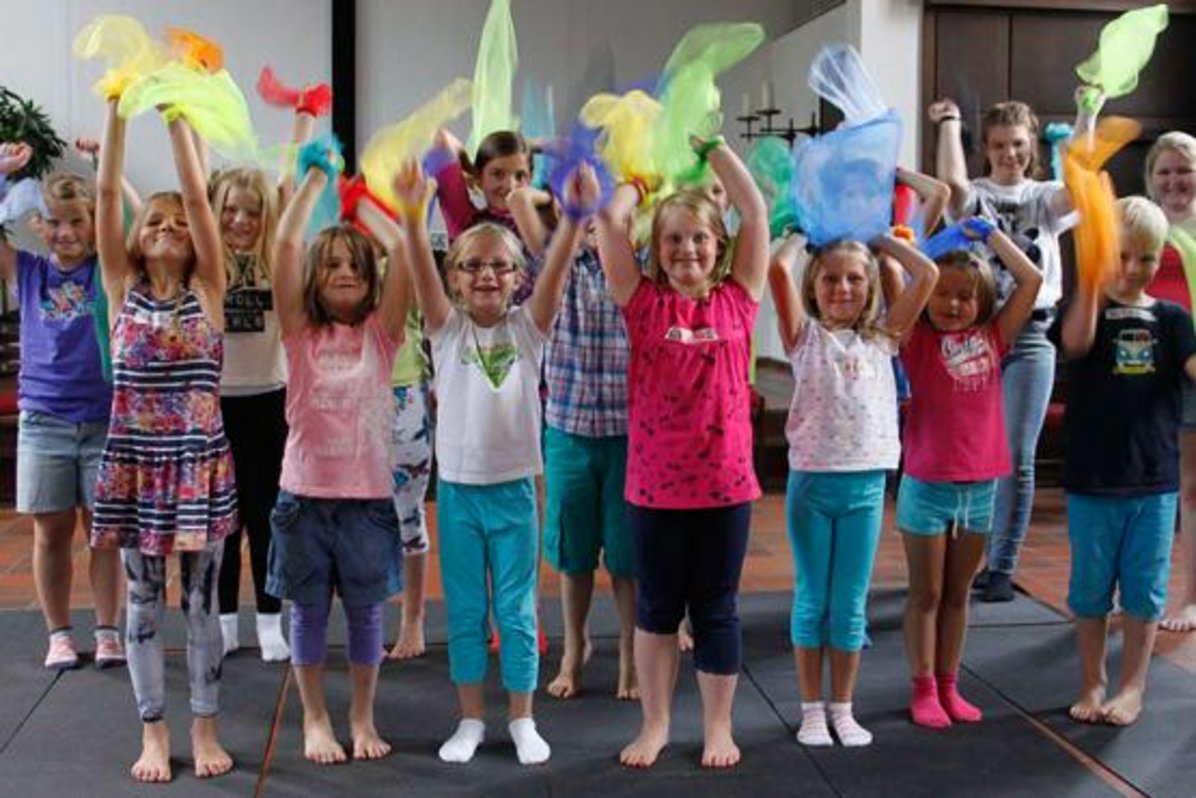Viele Kinder aus der OGS stehen nebeneinander und werfen bunte Tücher in die Luft.