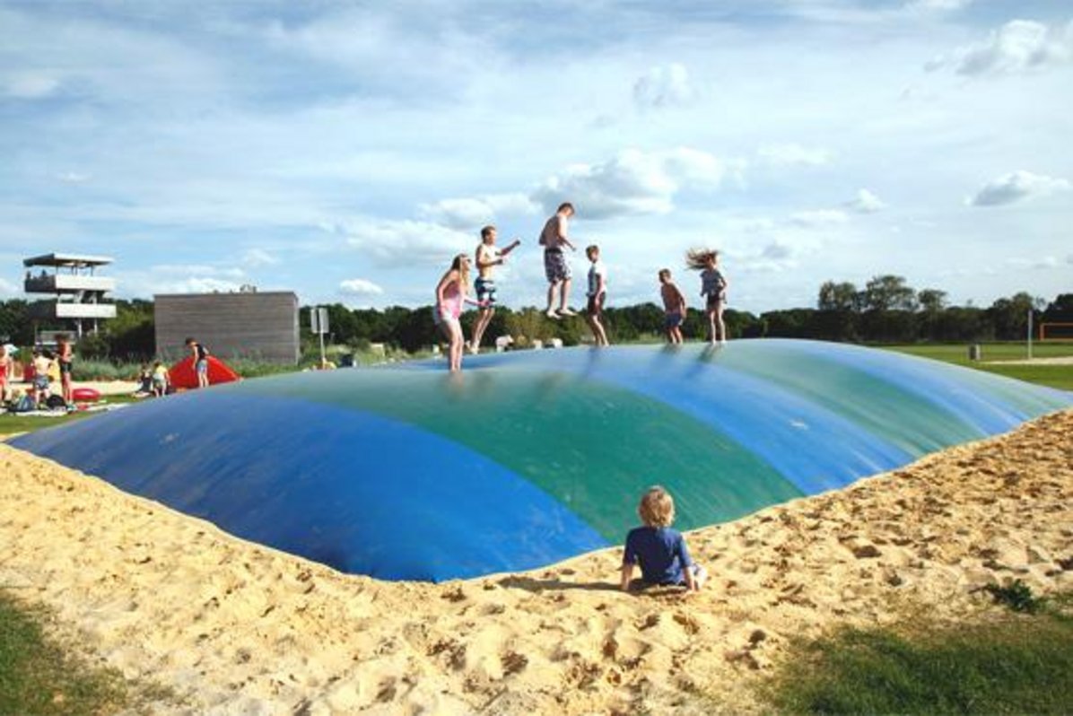 Kinder springen auf dem gelb-grünen Hüpfkissen im Naturbad