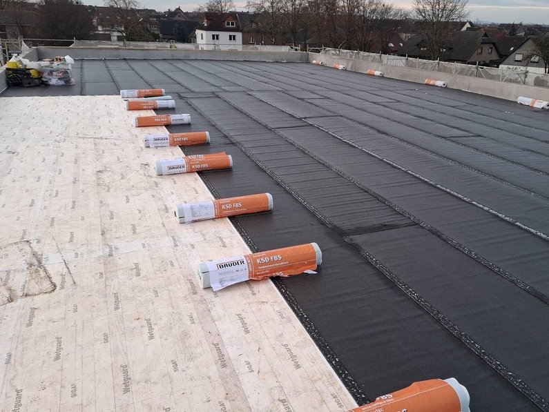 Auf dem Foto ist das Dach der Sporthalle von Außen zu sehen. Darauf wird aktuell eine Lignotrend-Decke verlegt.