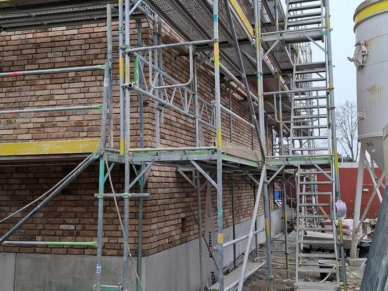 Auf dem Foto ist die Verblendung der Sporthalle zur Richtung der Feuerwehr zu erkennen. Der Klinker wurde bereits eingesetzt, drumherum stehen noch viele Gerüste und Baumaterial.