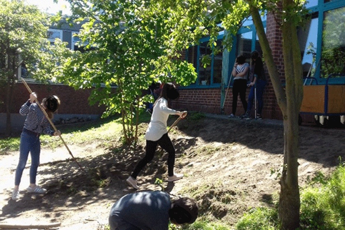 Auf dem Bild sind vier Schülerinnen zur erkennen, die mit Gartenwerkzeug den Garten hinter der Wolfhelmschule aufarbeiten.