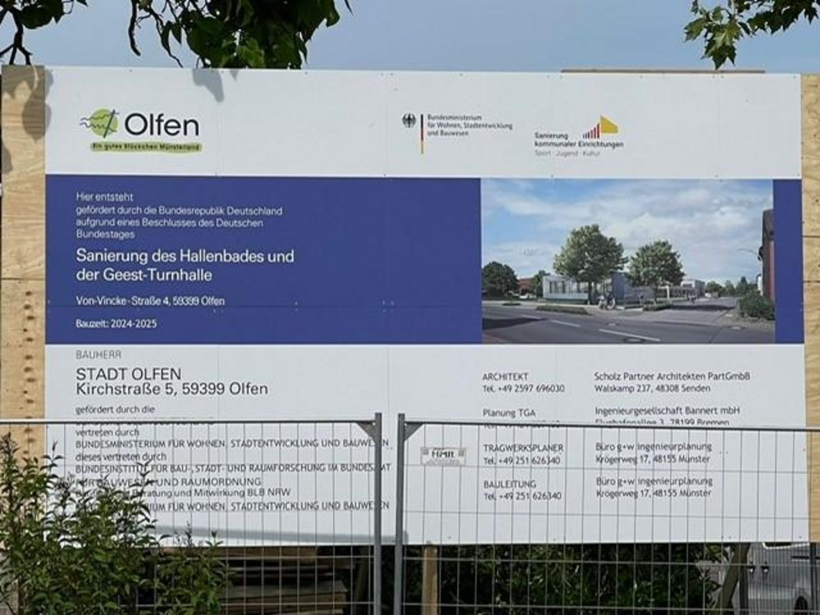 Auf dem Foto ist das große Schild zum Vorhaben der Sanierung des Hallenbades und der Geest-Turnhalle zu sehen. Dieses steht vor zwei Bauzäunen. Auf dem Schild, sind die Ansprechpartner für Bauherrn, Architekt, Planung und Bauleitung aufgeführt.