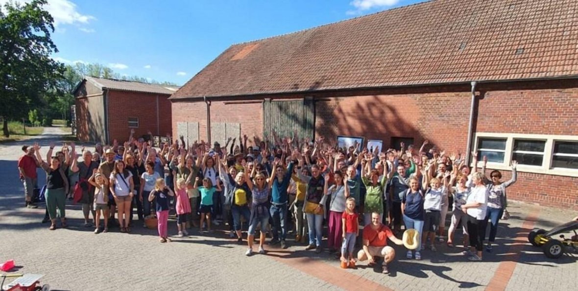 Mitglieder der SoLaWi Olfen e. V. auf dem Hof von Mehring. Über 100 Personen halten die Hände nach oben und stehen zusammen.