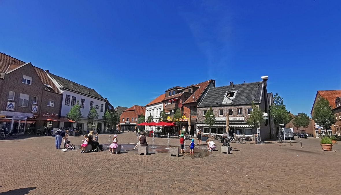 Zu sehen ist der Marktplatz in Olfen. Am Brunnen sitzen mehrere Personen mit Kindern.