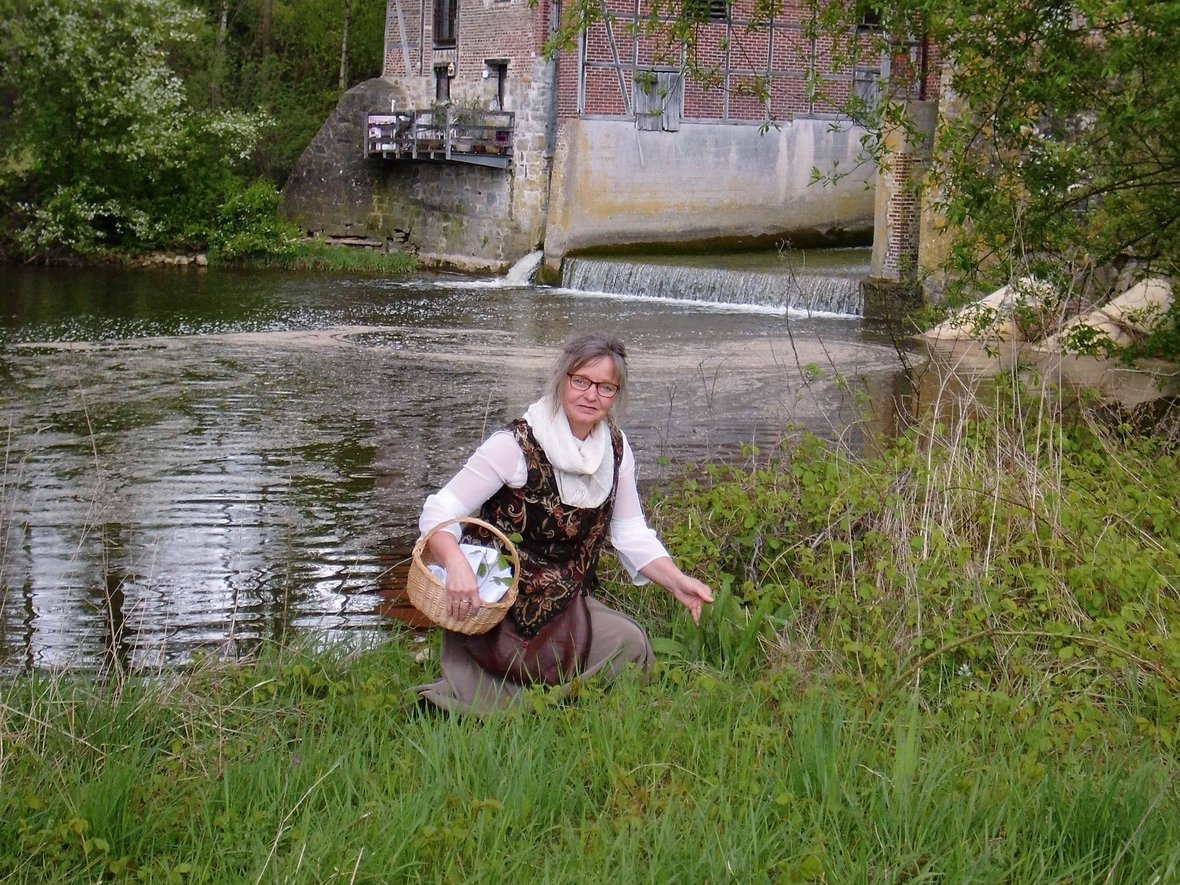 Barbara Zuz bietet als Naturkundeführerin Kräuterführungen in der Steveraue an. Auf dem Foto kniet sie mit einem Korb in der Wiese vor der Füchtelner Mühle.