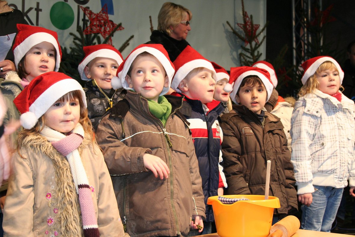 Mehrere Kinder stehen auf der Bühne des Adventsmarktes in Olfen und tragen rote Nikolausmützen.