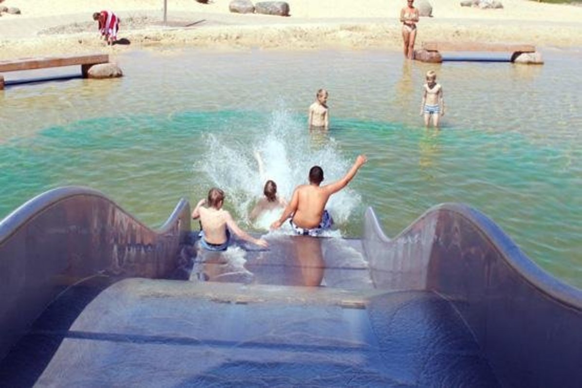 Drei Kinder rutschen die Wellenrutsche im Naturbad herunter und landen im Wasser.