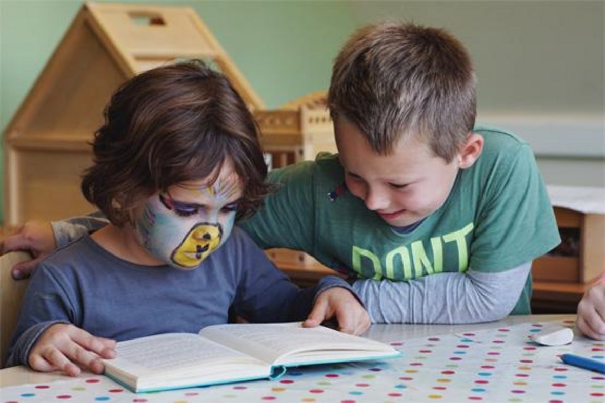 Zwei Kinder sitzen am Tisch und lesen gemeinsam in einem Buch.