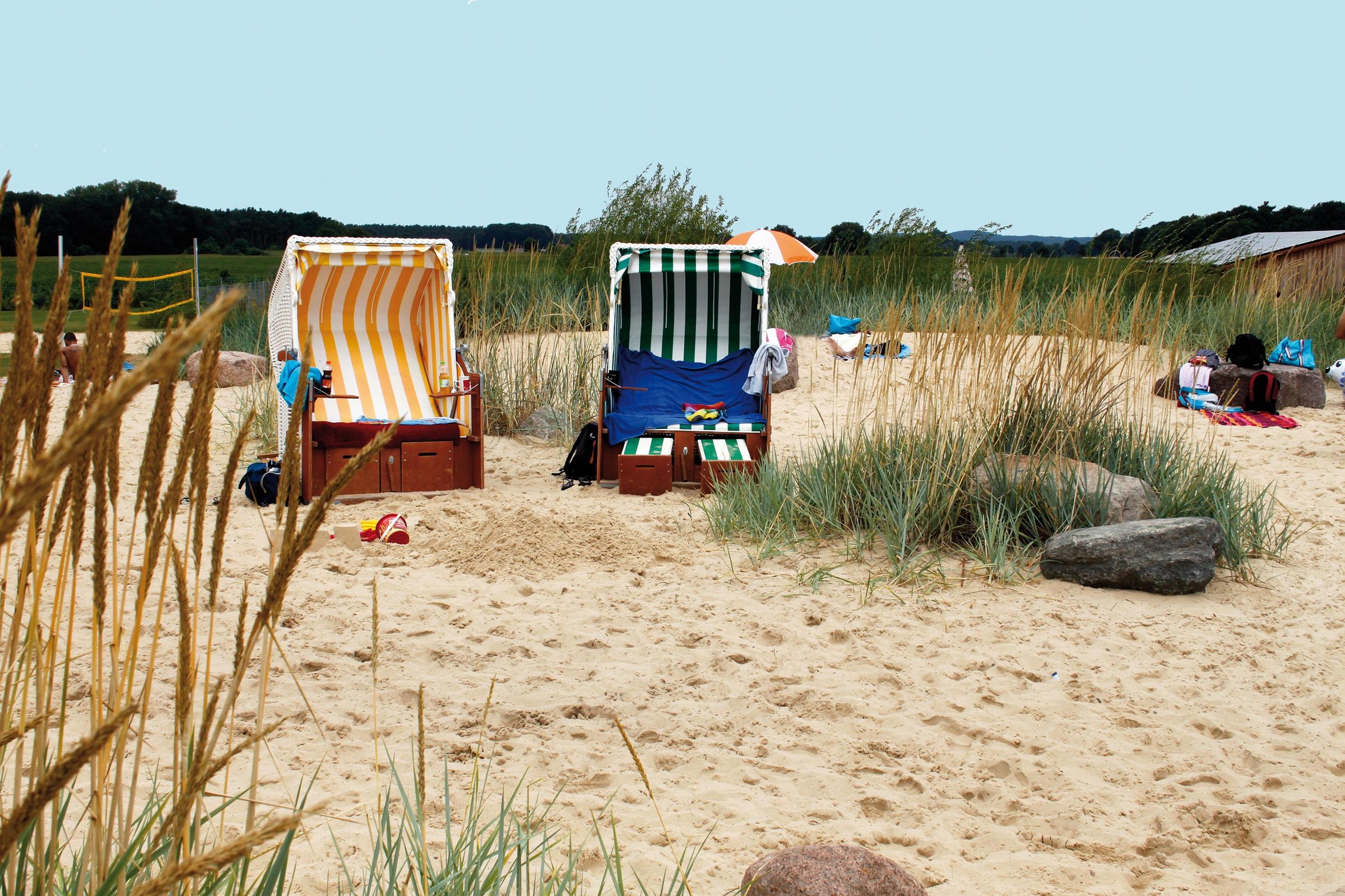 Ein gelb-weiß gestreifter und ein grün-weiß gestreifter Strandkorb stehen im Strandbereich des Naturbades.