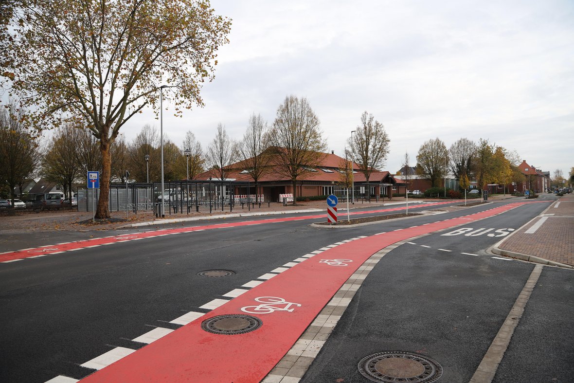 Das Bild zeigt den Bereich vor der Stadthalle in Olfen. Auf der Straße sind rote Fahrradwege zu erkennen. Im Hintergrund sind die Abstellboxen für Fahrräder zu sehen.