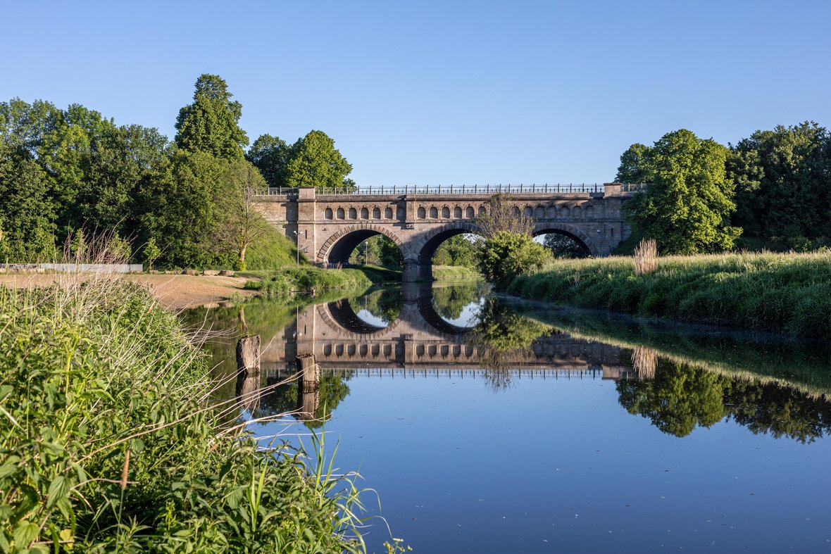 Auf dem Foto sieht man die Dreibogenbrücke und den davor liegenden Flussstrand. Die Stever fließt durch die Brücke hindurch.