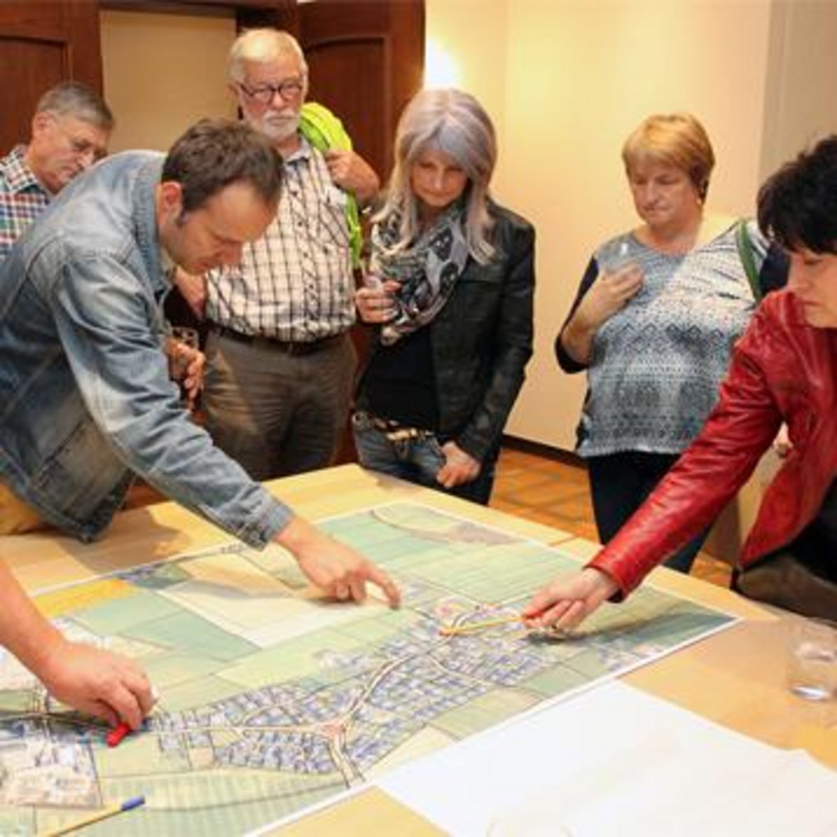 Auf dem Bild sind 6 Personen zu sehen, die um einen Tisch mit Plänen herum stehen und sich zum Dorfentwicklungskonzept Vinnum beraten.