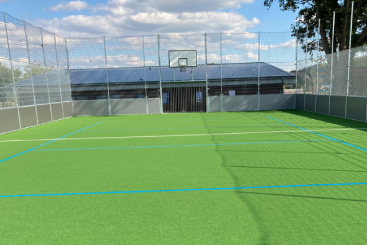 Das Multifunktionales Spielfeld in Vinnum ist eine eingezäunte Spielfäche mit grünem Boden. Zu sehen ist ein Tor, das für Fuß- oder Handball genutzt werden kann und ein Basketballkorb.