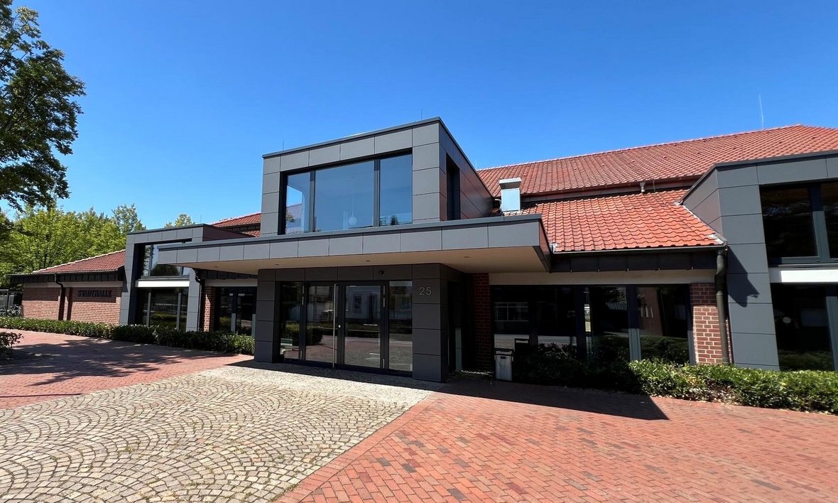 Außenansicht der Stadthalle Olfen mit modern gestaltetem Eingangsbereich, rotem Ziegeldach und gepflastertem Vorplatz bei blauem Himmel.