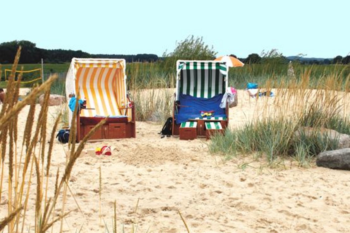 Das Foto zeigt einen gelben-weiß gestreiften und einen grün-weiß gestreiften Strandkorb im Sand- und Dünenbereich des Naturbades.