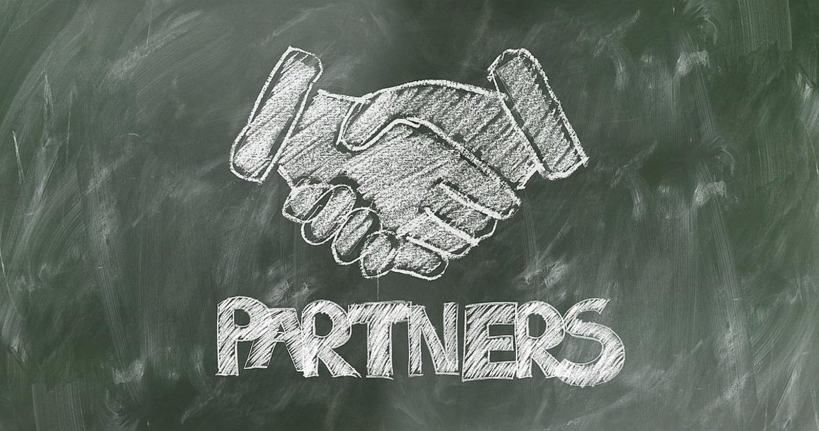 Die Grafik zeigt eine Tafel auf der mit Kreise zwei Hände, die sich die Hand geben und das Wort PARTNERS gezeichnet wurde.
