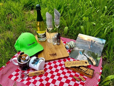Auf einer roten Picknickdecke auf einer Wiese wurden einige Souvenirs platziert: Tassen, Esel, Flaschenöffner, Servierbrett, Frühstücksbrettchen, Sekt und Sektgläser, Domino-Spiele, Kindermesser.