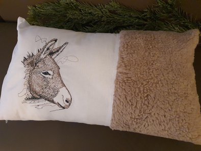 Das Plüschkissen ist zur Hälfte weiß und zur Hälfte in hellbrauner Felloptik. Auf der weißen Hälfte wurde der Kopf eines Esel gestickt.