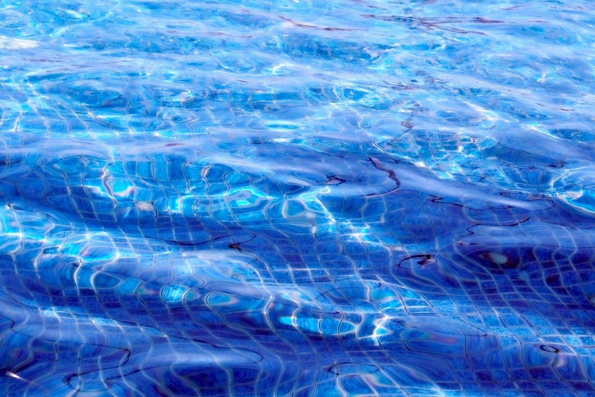 Das Foto zeigt Wasser in einem Schwimmbecken. Der Boden des Schwimmbeckens ist blau gefließt.